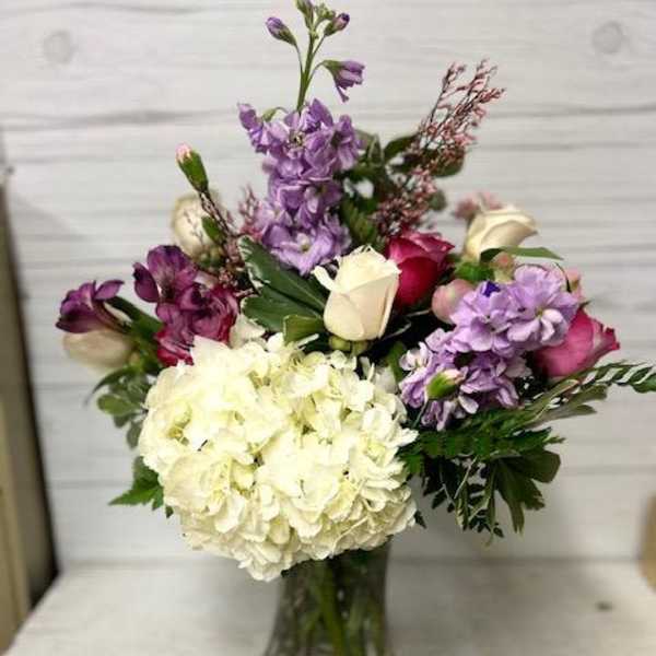 Mixed bouquet of white hydrangea, purple flowers, and roses in a glass vase