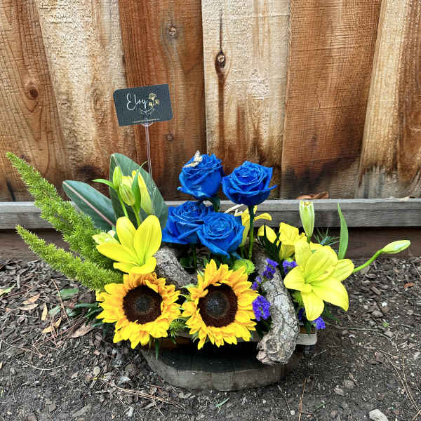 Arrangement of blue roses and yellow lilies with sunflowers in a rustic container