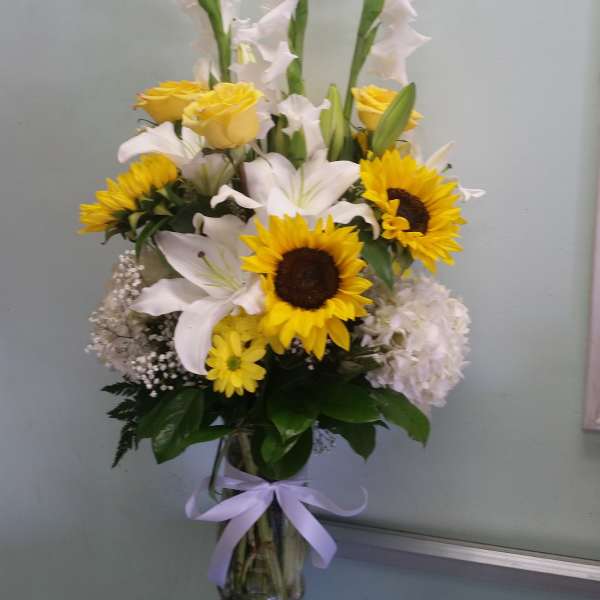 Tall bouquet of sunflowers, white lilies, and yellow roses in a glass vase
