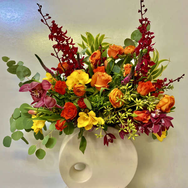 Bright mixed flower arrangement in a white vase with red, orange, yellow, and purple blooms.