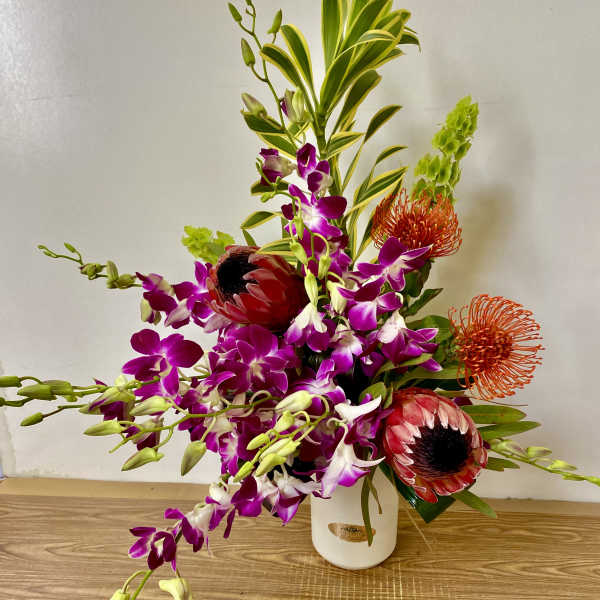 Tropical floral arrangement with purple orchids and red protea in a white vase