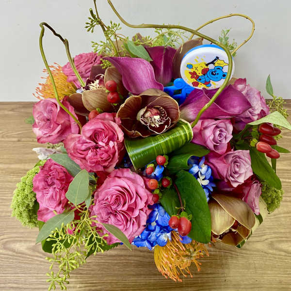 Pink and purple floral arrangement with orchids and roses in a low container