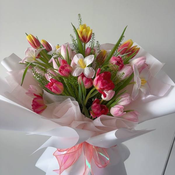Bouquet of pink and yellow tulips with white flowers wrapped in pale pink paper