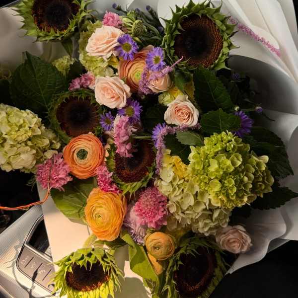 Mixed bouquet with sunflowers, roses, ranunculus, and hydrangeas wrapped in white paper