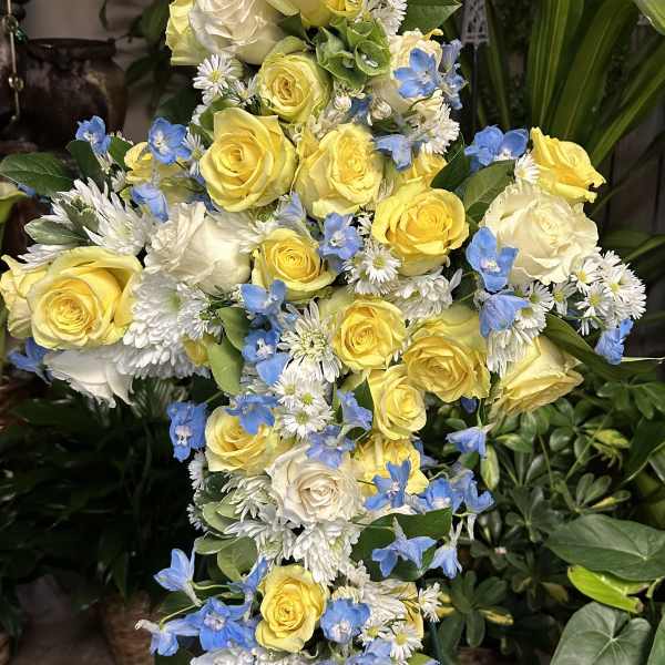 Tall floral spray of yellow and white roses with blue accent flowers