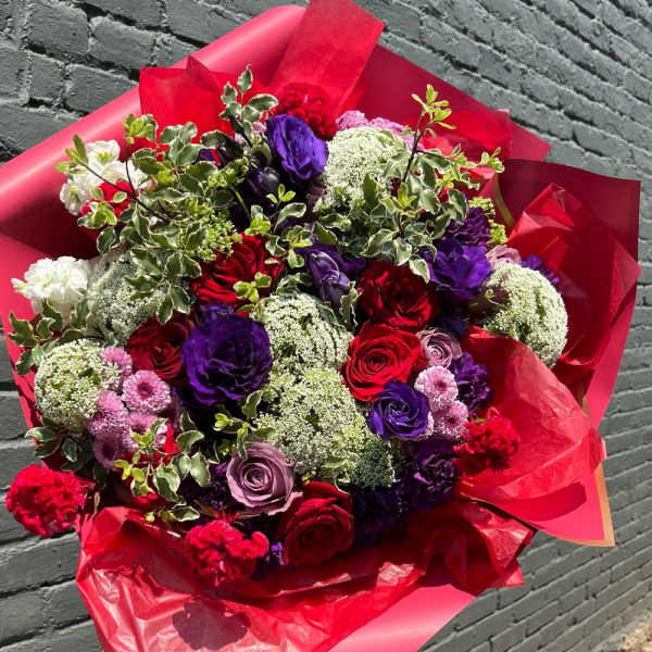 Large bouquet of red, purple, and pink flowers wrapped in red paper