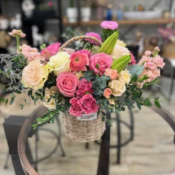 Basket arrangement of pink and cream roses with lilies