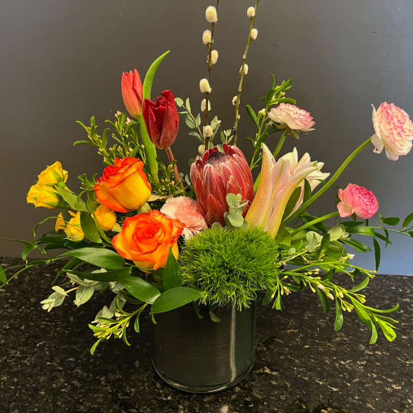 Mixed bouquet with roses, tulips, and a protea in a glass vase