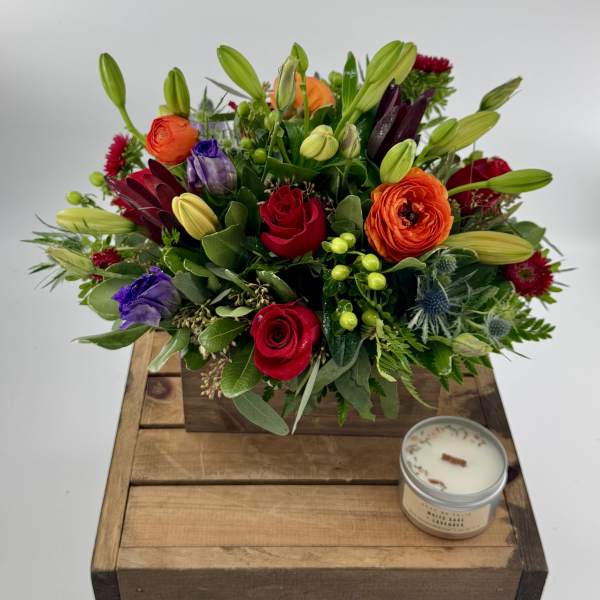 Mixed bouquet with roses, lilies, and purple blooms in a wooden box beside a candle