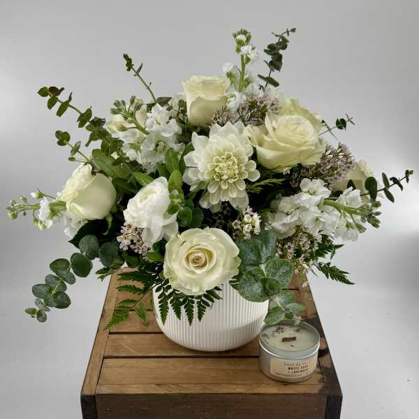 White rose arrangement in a ribbed vase with a small candle beside it