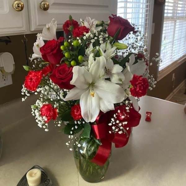 Red roses and white lilies in a glass vase with a red ribbon