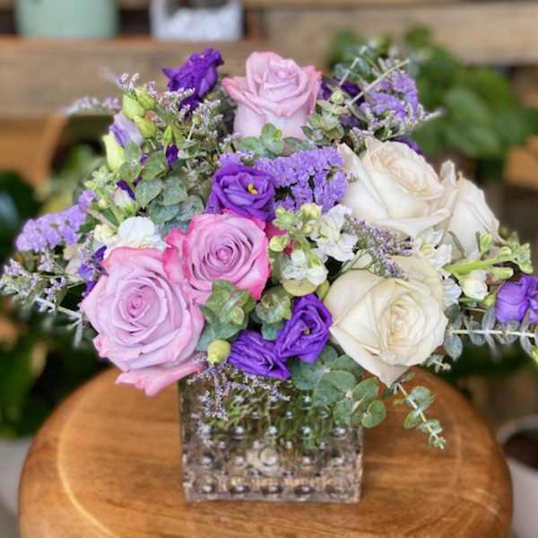 Pink, white, and purple roses arranged in a clear square vase.