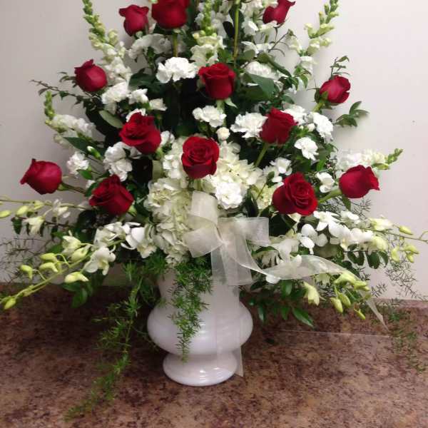 Tall arrangement of red roses and white flowers in a white vase with a sheer ribbon
