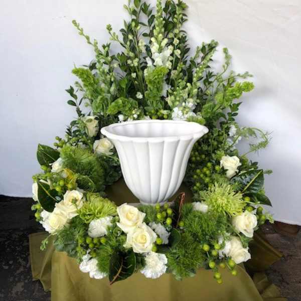 White urn surrounded by green and white floral arrangement