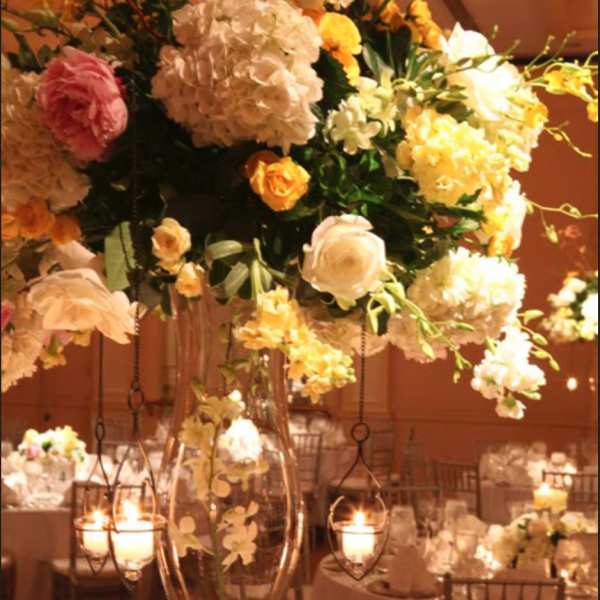 Tall floral centerpiece in a clear glass vase with hanging candle holders