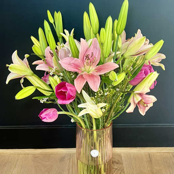 Pink and white lilies with tulips in a tall glass vase