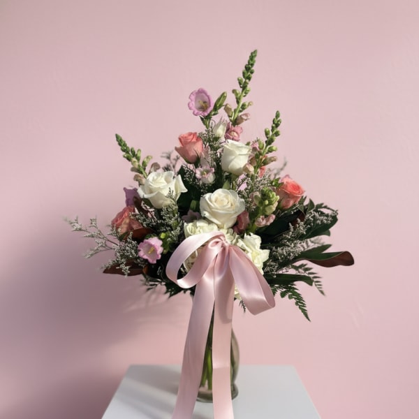Pink and white rose bouquet in a glass vase with a satin ribbon