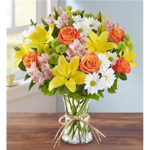 Mixed bouquet of yellow lilies, orange roses, and white daisies in a glass vase