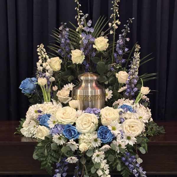Sympathy floral arrangement with white roses, blue flowers, and a metal urn
