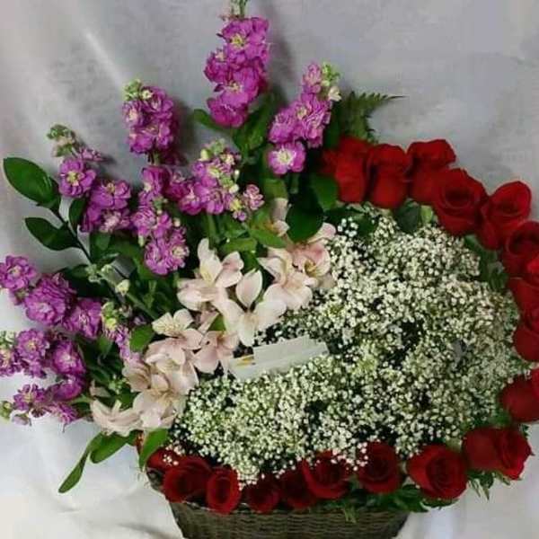 Basket arrangement of red roses, purple stock, and white baby's breath