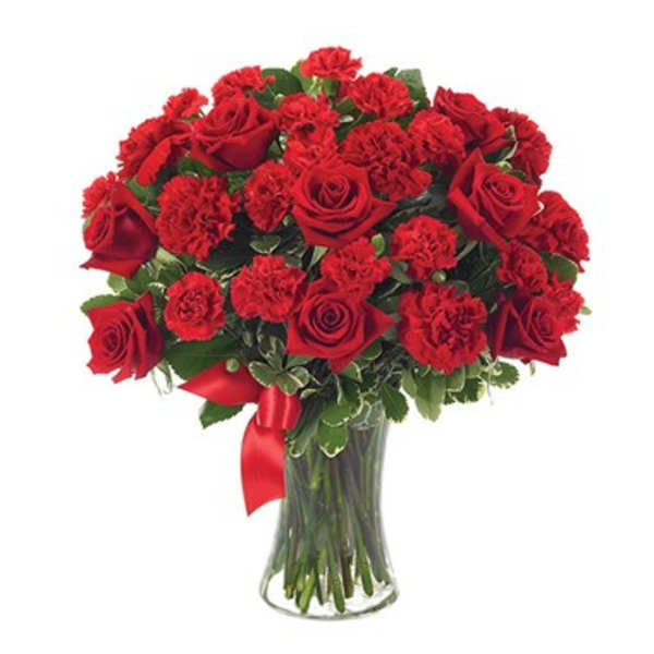 Red roses and carnations in a clear glass vase with a red ribbon