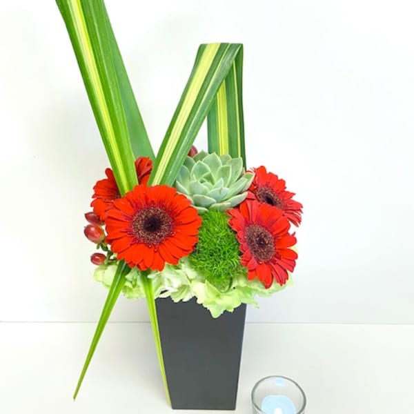 Red gerbera daisies and succulents in a black vase with a candle nearby