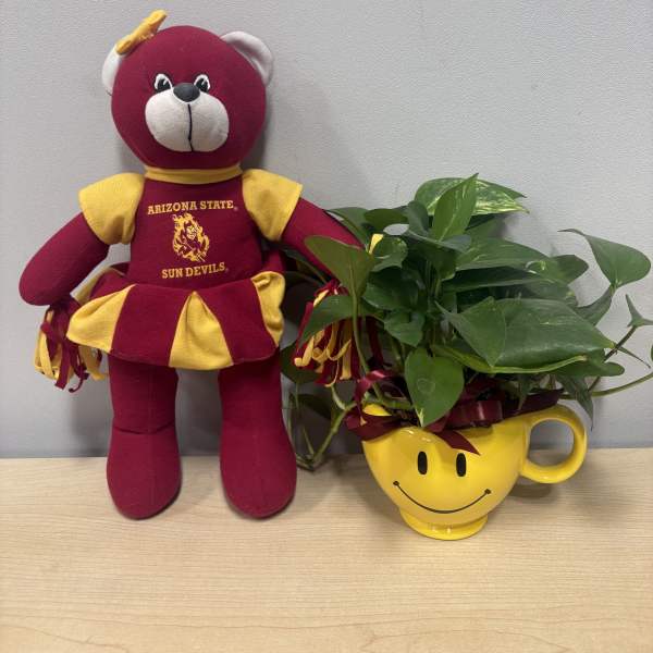 Plush bear beside a leafy plant in a yellow smiley-face mug