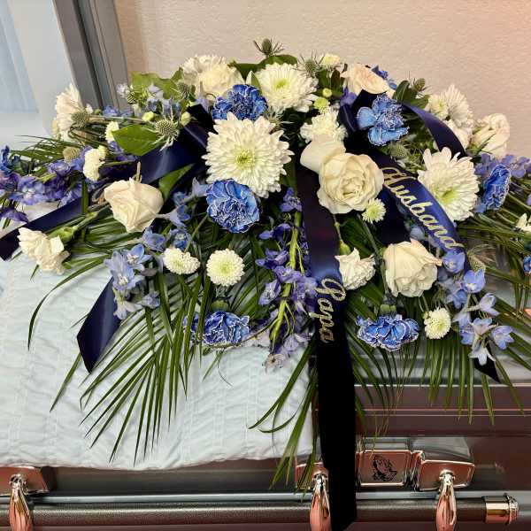 White and blue floral casket spray with ribbon on a coffin