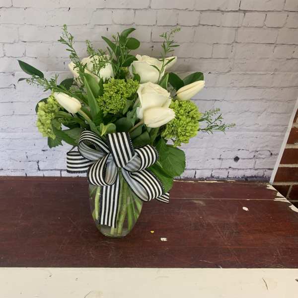 White roses and tulips in a glass vase with a striped ribbon