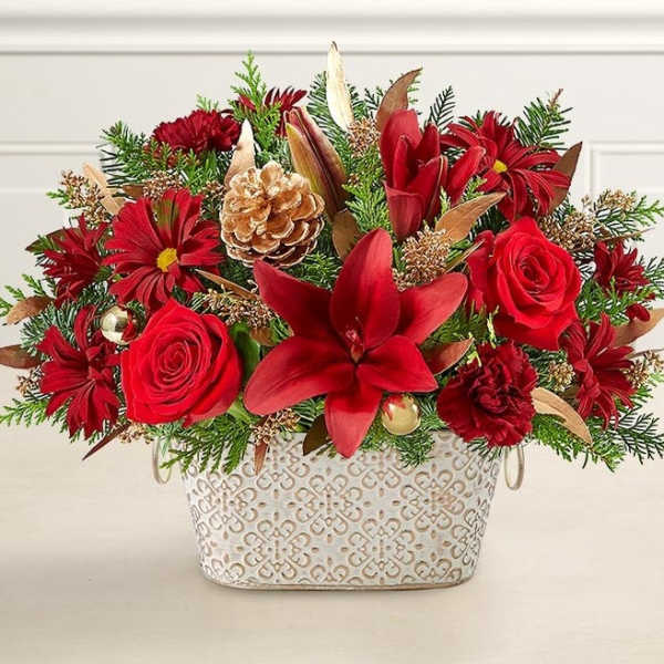 Red floral arrangement in a patterned white container with a pinecone accent