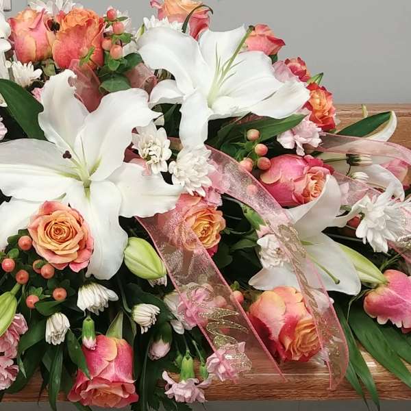 Large floral casket spray with white lilies, pink roses, and ribbon accents