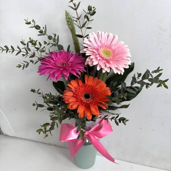 Gerbera daisies in pink, orange, and magenta in a vase with a pink ribbon