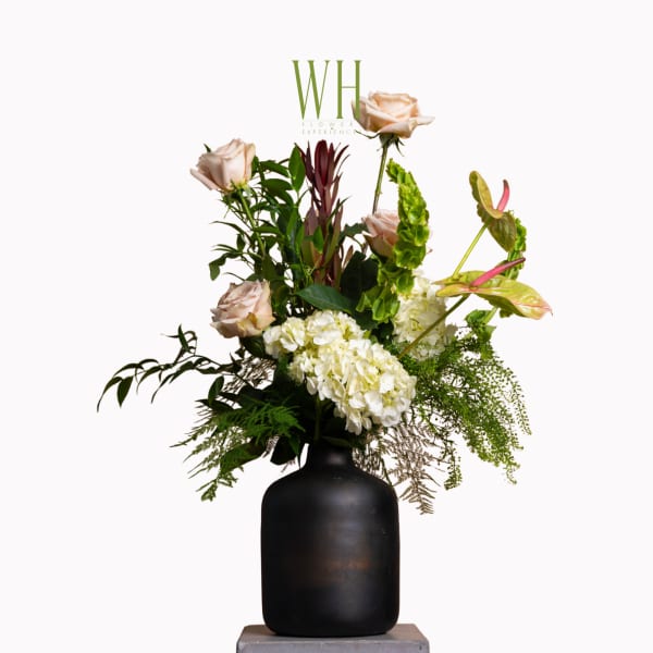 Floral arrangement with pale roses, white hydrangea, and tropical blooms in a black vase