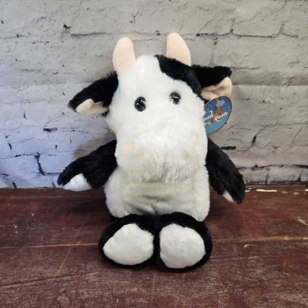 Black-and-white plush cow sitting upright on a wooden surface