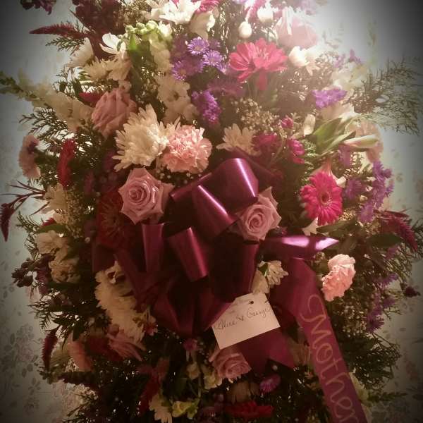 Large standing floral spray with pink, white, and purple blooms and a magenta ribbon