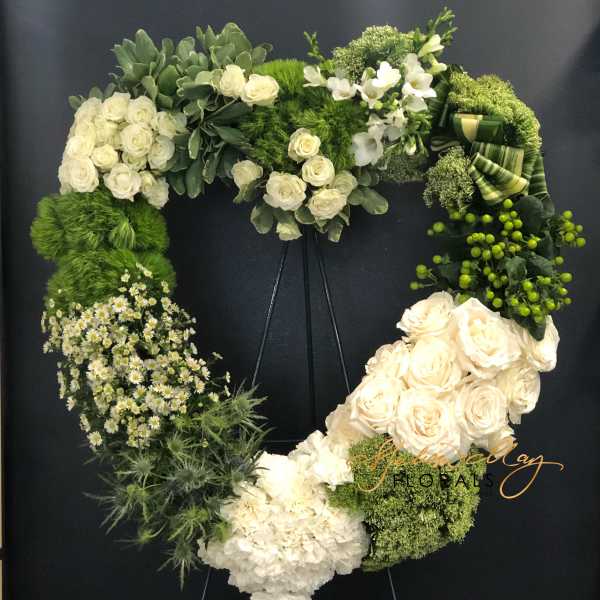 Heart-shaped floral wreath with white roses and green blooms on a stand