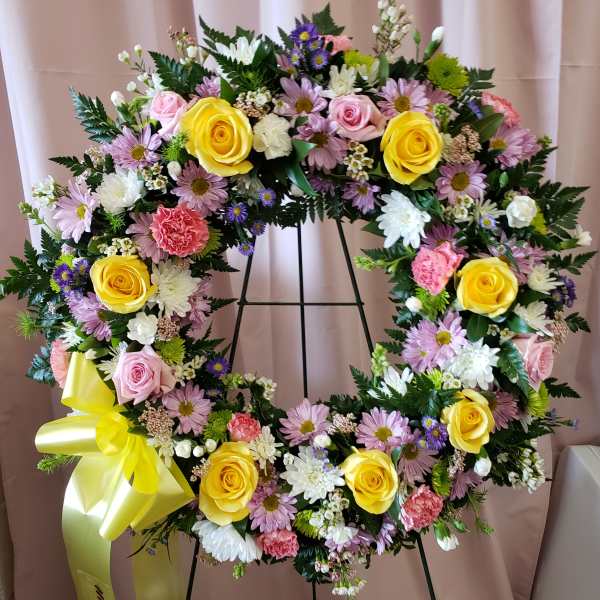 Large floral wreath with yellow roses, pink flowers, and a yellow ribbon