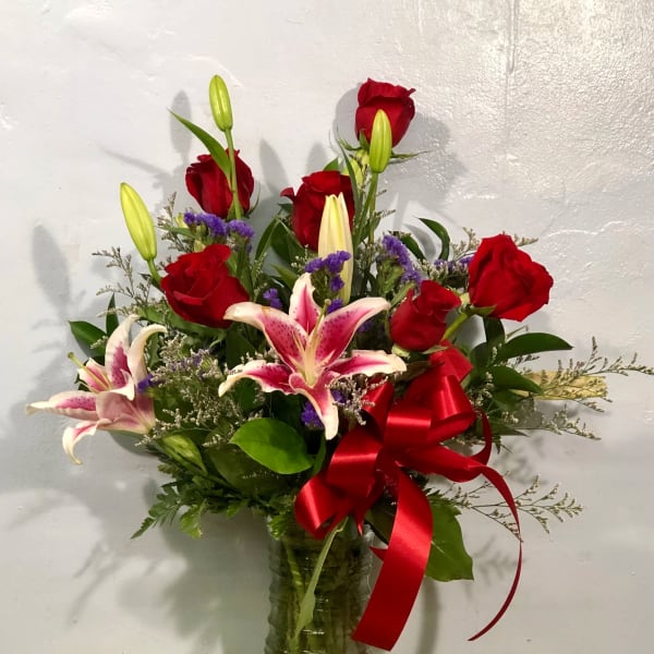 Bouquet of red roses and pink lilies in a glass vase with a red ribbon