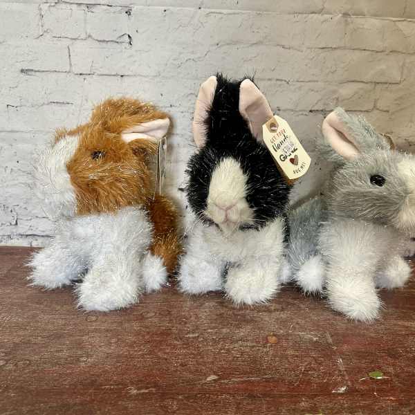 Three plush bunny figurines sit on a wooden surface.