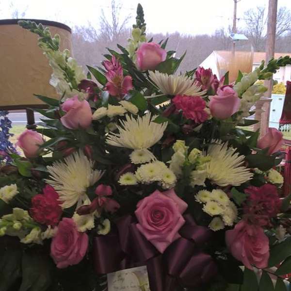 Pink roses and white spider mums arranged in a vase with a purple ribbon.