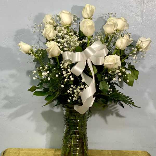 White roses arranged in a glass vase with a white ribbon