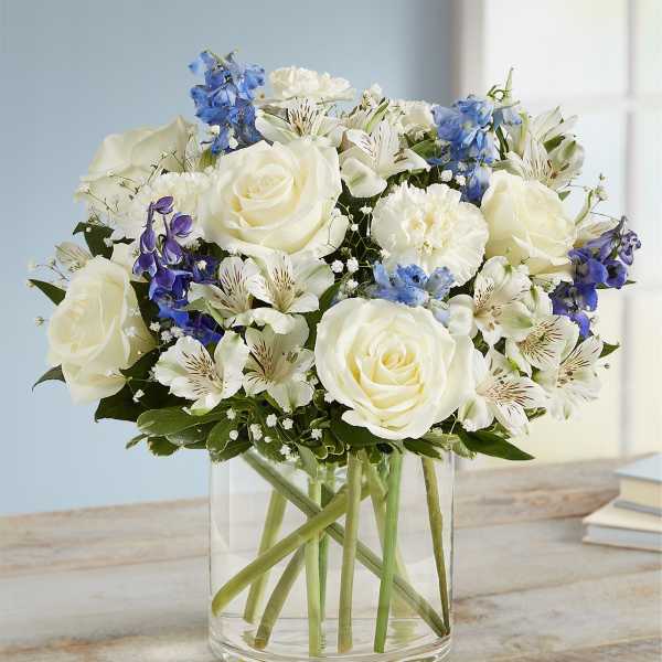 White roses and blue flowers arranged in a clear glass vase