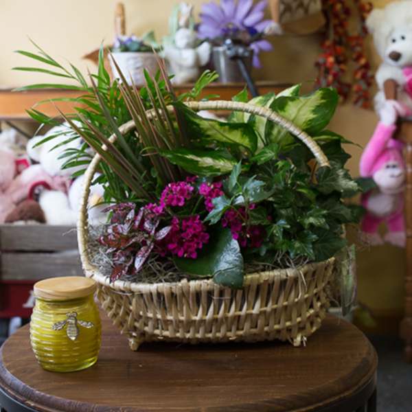 Basket arrangement with green foliage and pink flowers beside a yellow jar candle