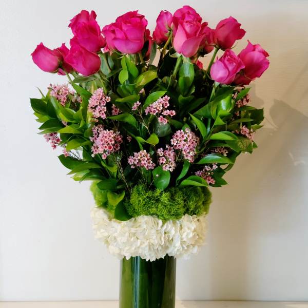 Pink roses in a tall glass vase with white and green accents