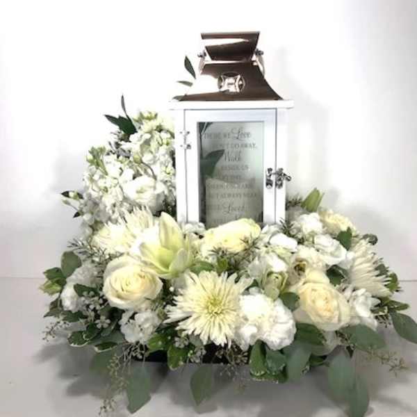 White floral arrangement around a white lantern with a candle inside