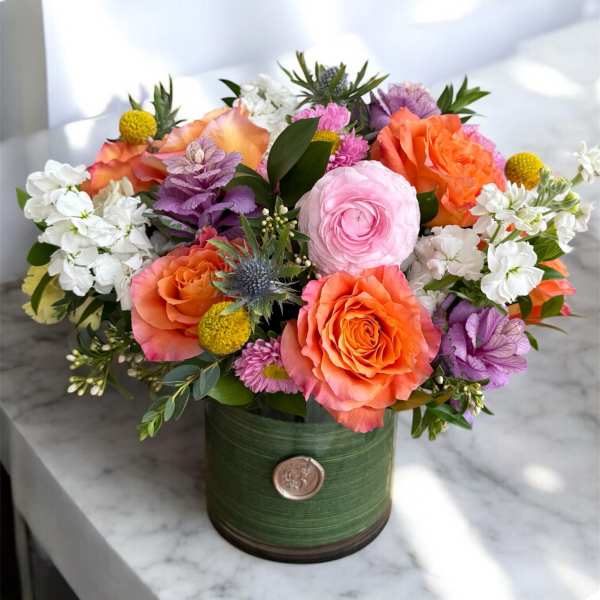Colorful bouquet of roses, ranunculus, and white blooms in a green container