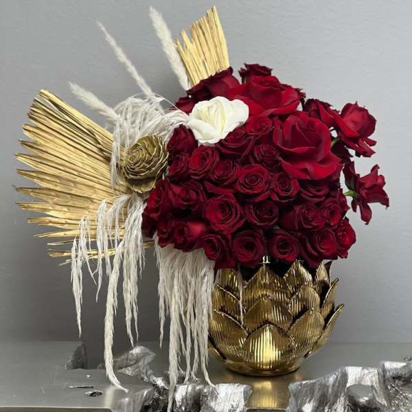 Red roses arranged with gold decorative accents in a gold vase