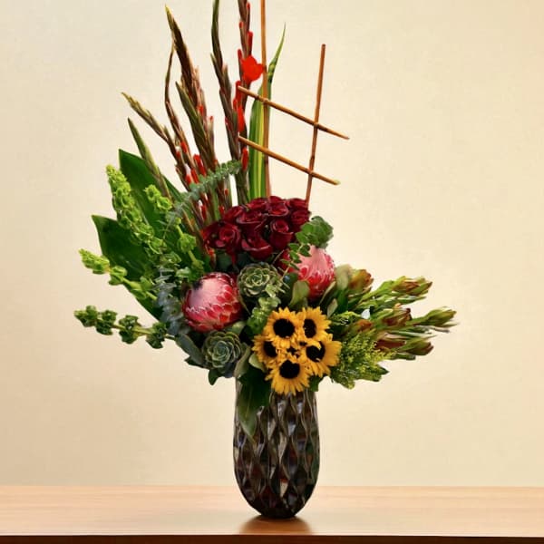 Tall mixed floral arrangement in a dark vase with red, yellow, and green blooms