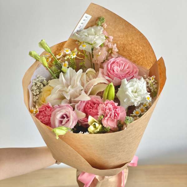 Hand-tied bouquet of pink and white flowers wrapped in brown paper