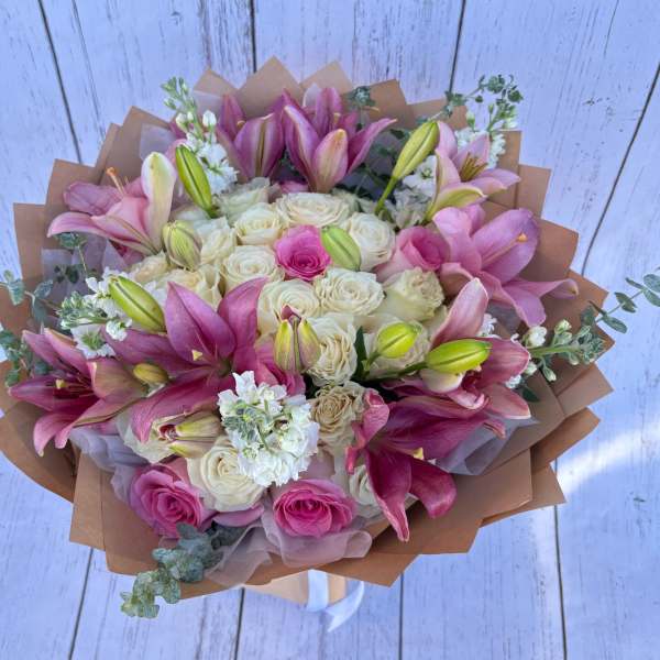 Bouquet of pink lilies and cream roses wrapped in brown paper